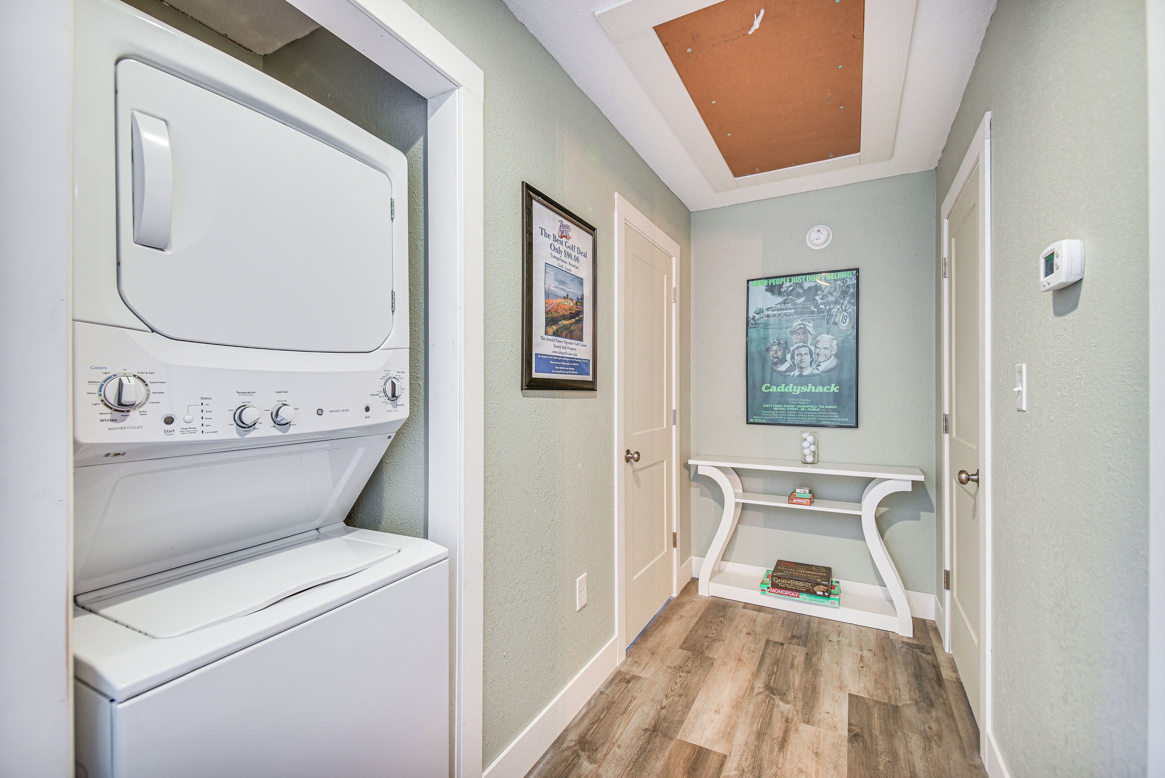 A laundry room with a front-loading washer and dryer, a small shelf with toiletries, and a poster on the wall.