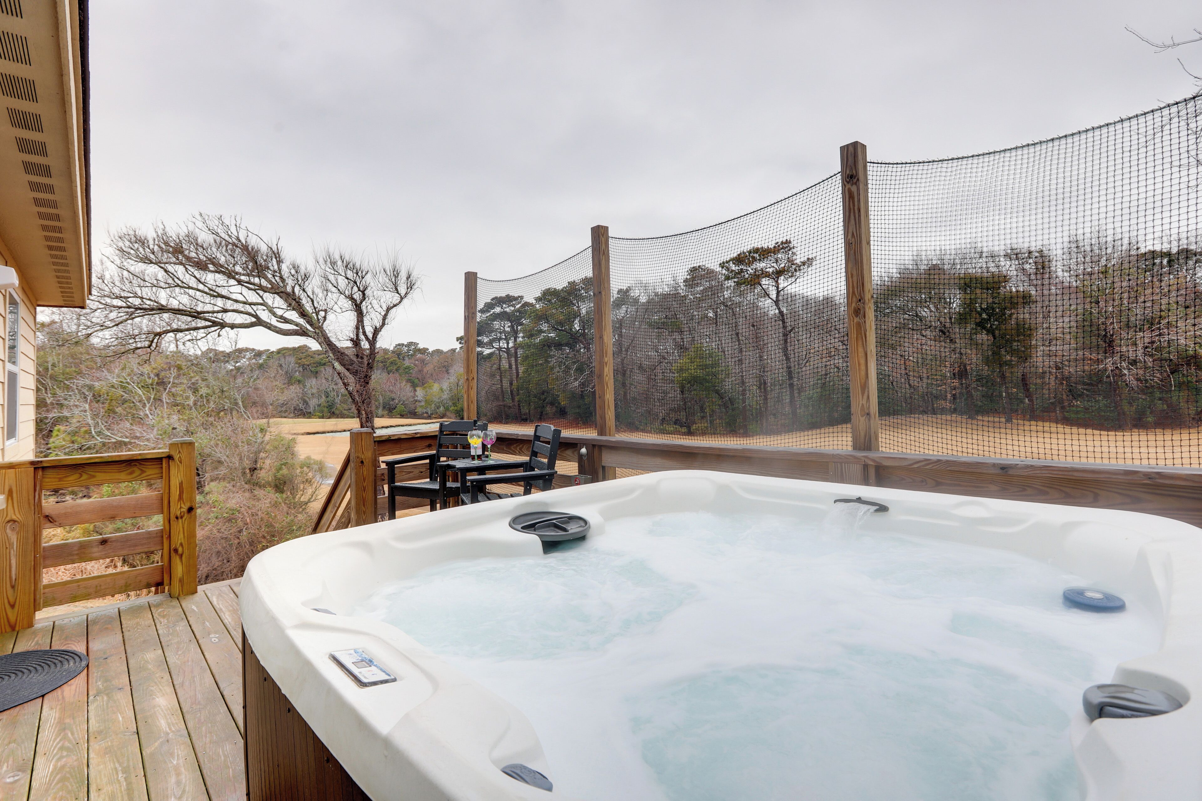 A hot tub on a wooden deck with a view of trees and a fence.