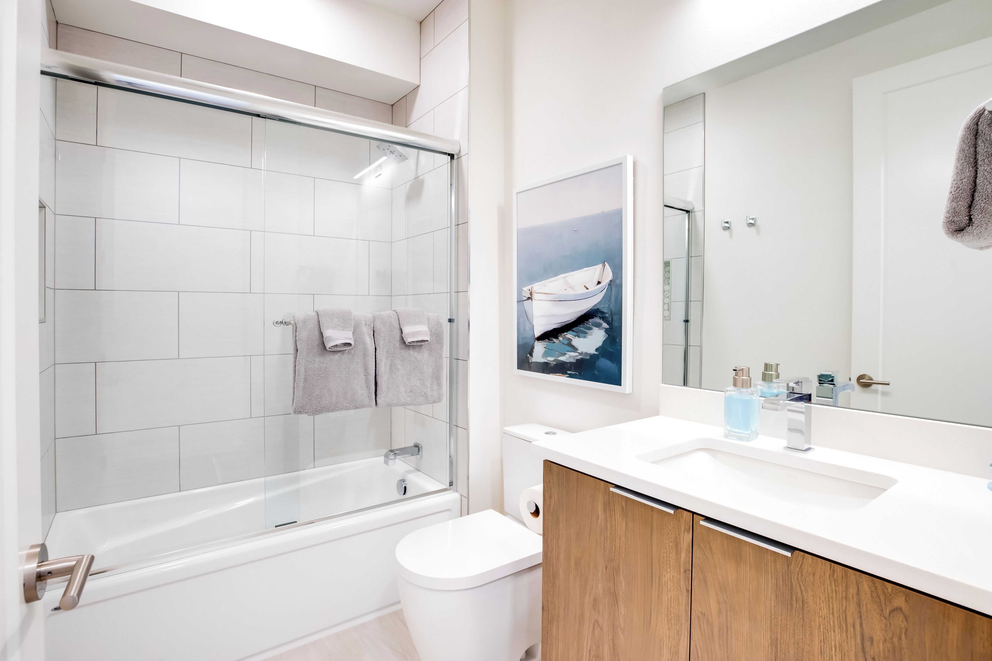 A modern bathroom with a glass-enclosed shower, a white toilet, and a wooden vanity with a sink.