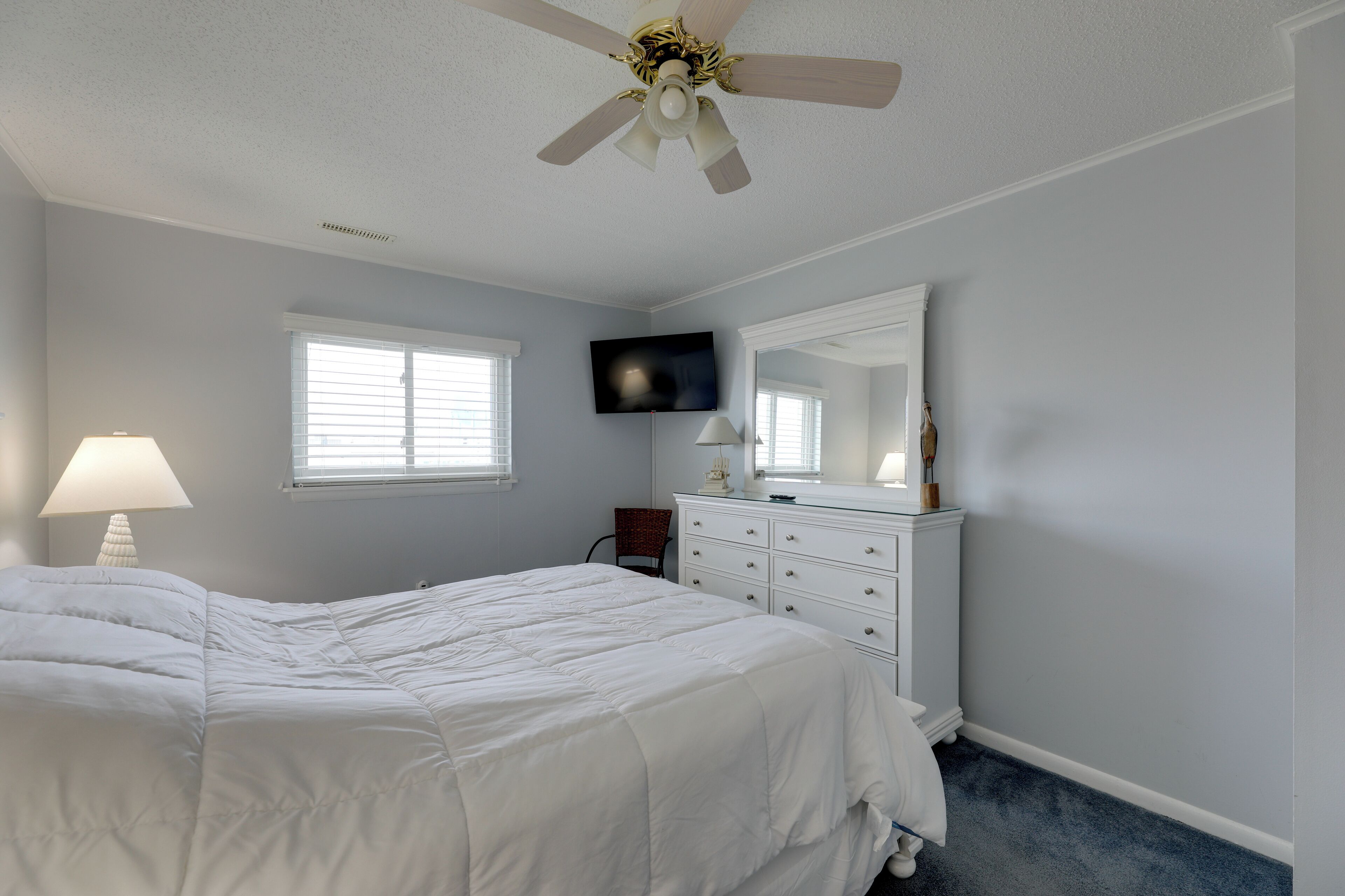 A bedroom with a bed, a dresser, a television, and a ceiling fan.