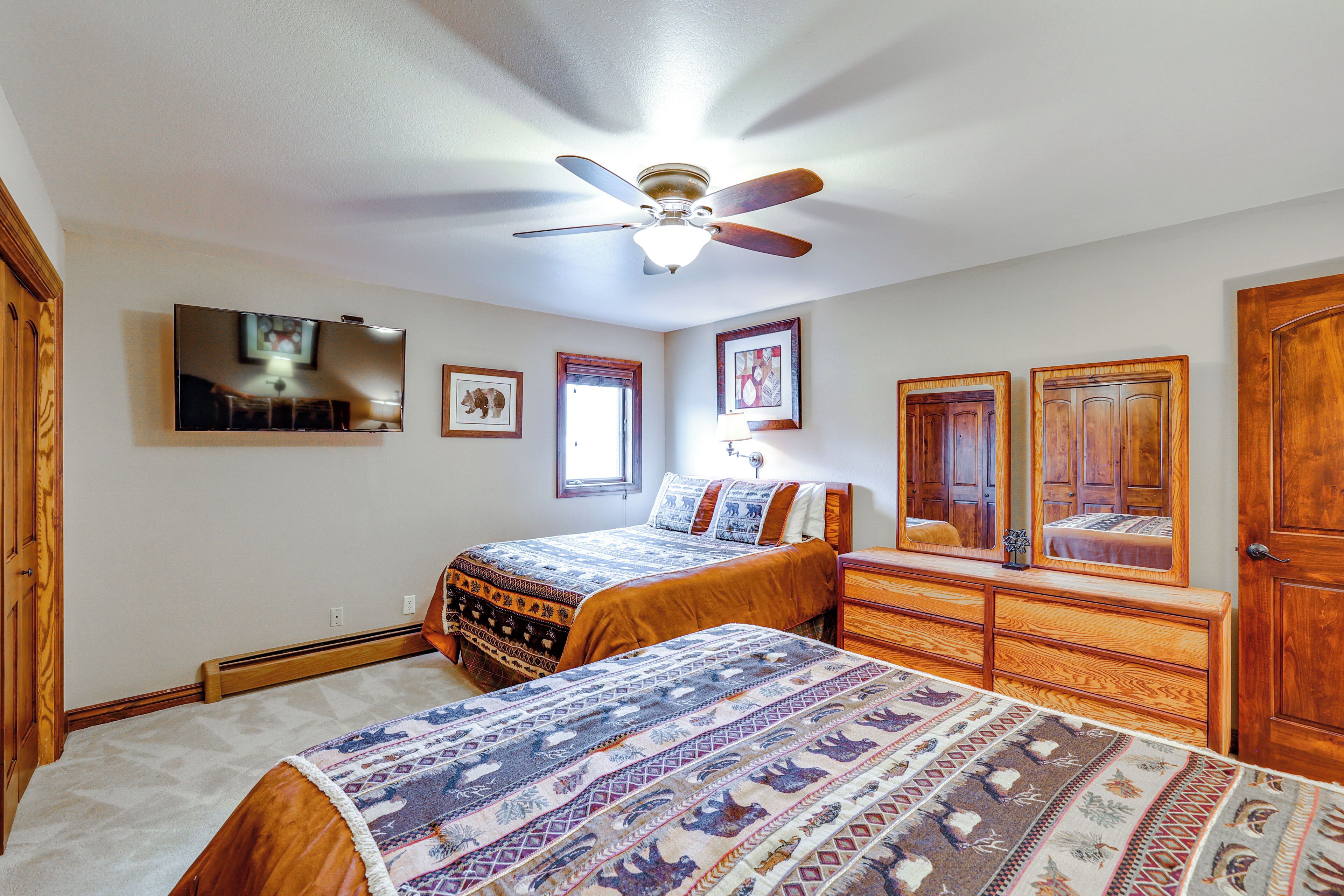 A bedroom with two beds, a ceiling fan, a dresser, and a mirror.