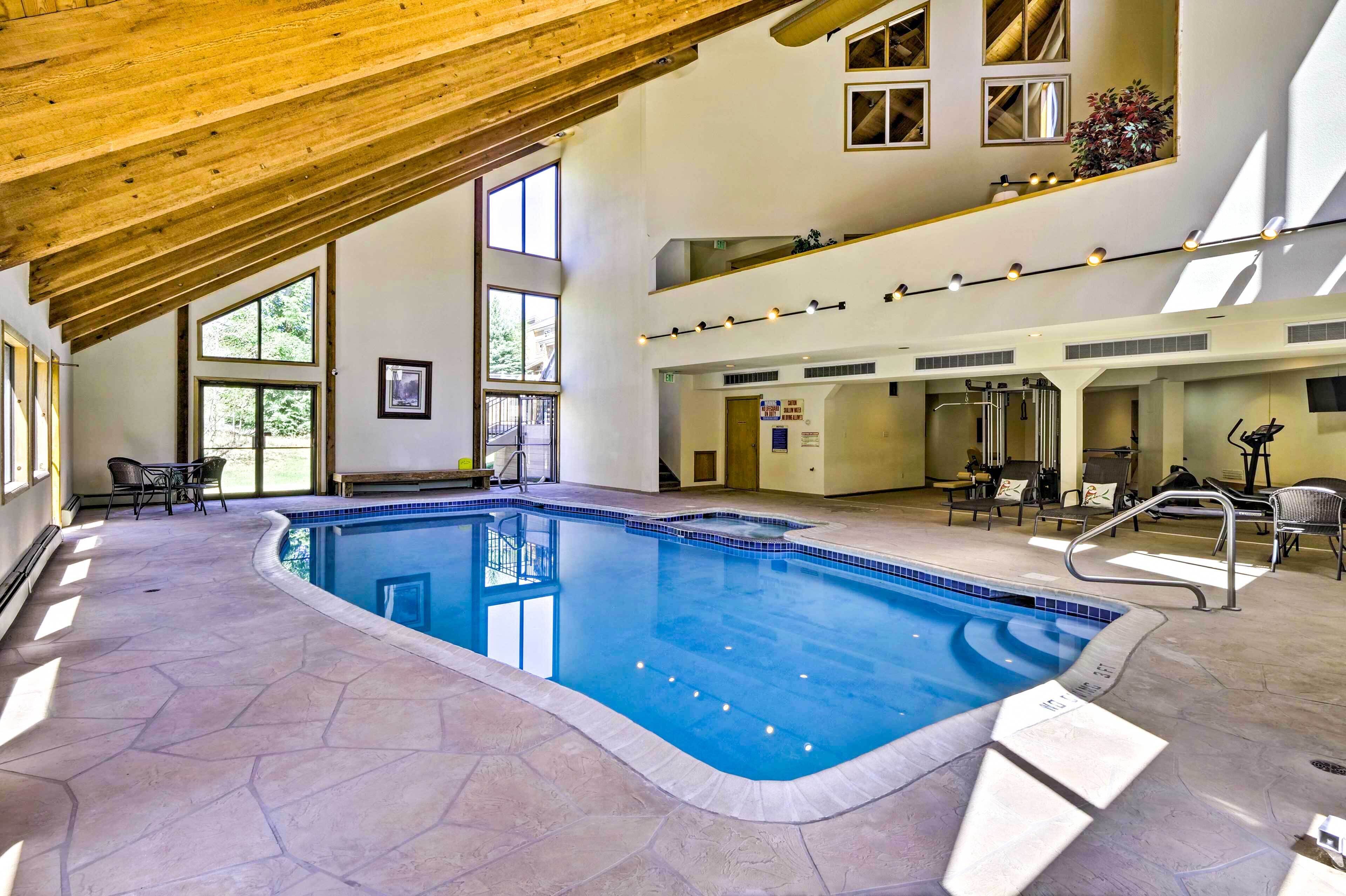 An indoor swimming pool with a stone floor, wooden ceiling beams, and multiple seating areas.