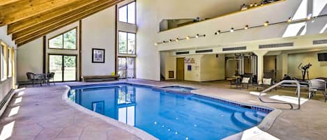 Una piscina interior con suelo de piedra, vigas de madera en el techo y varias zonas de descanso.