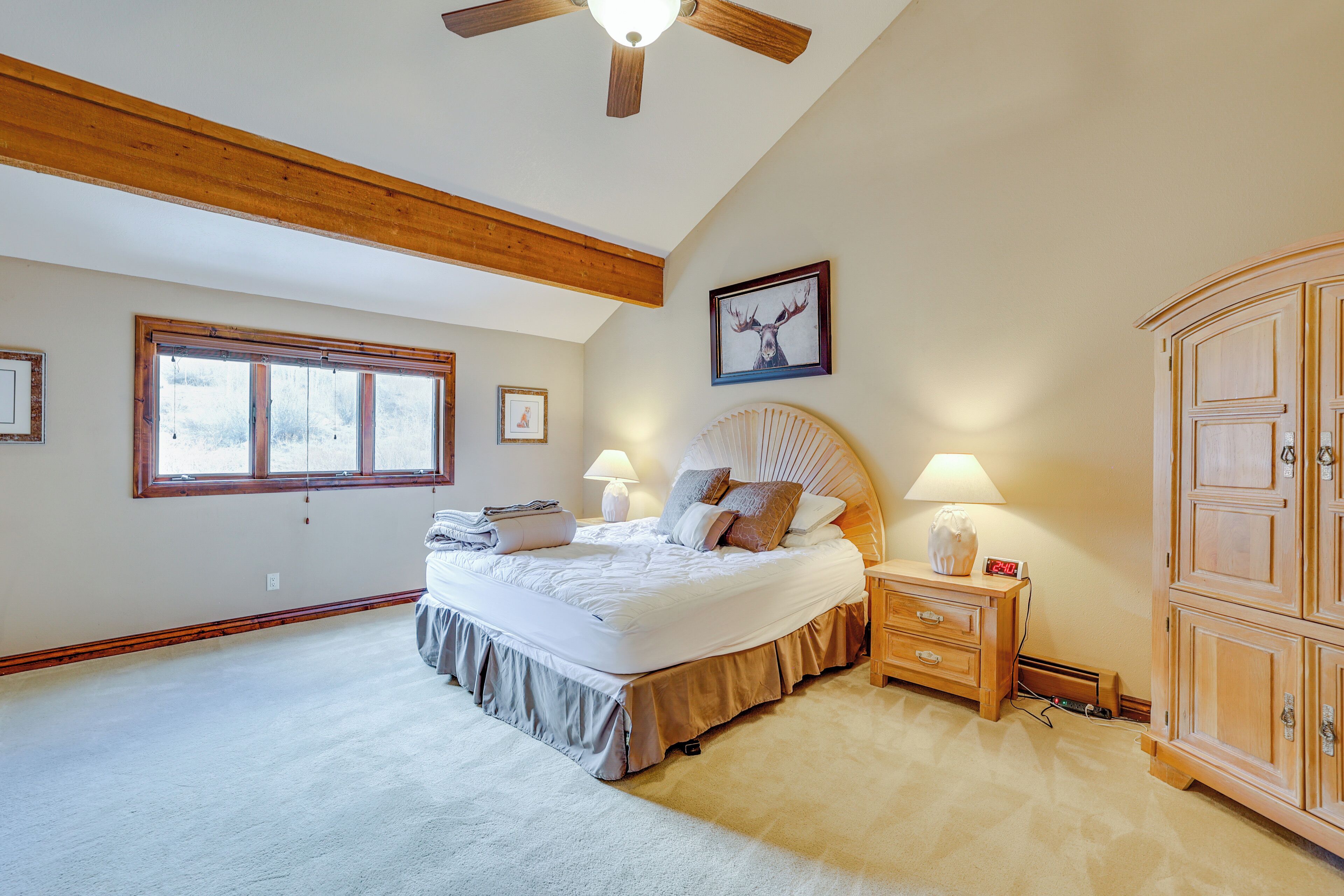 A bedroom with a large bed, wooden headboard, a ceiling fan, a window, and a wooden wardrobe.