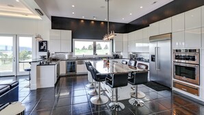 A modern kitchen with a central island, stainless steel appliances, and a large window providing a view of the outdoors. - Motorcycle-themed Home in Spearfish w/ Hot Tub! (Spearfish)