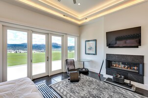 A modern bedroom with a large bed, a fireplace, and a view of a green landscape through large windows.