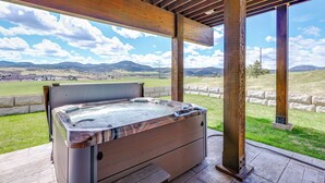 A hot tub in an outdoor covered area with a view of a grassy field and mountains. - Motorcycle-themed Home in Spearfish w/ Hot Tub! (Spearfish)