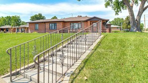 A residential building with a staircase leading to the entrance, surrounded by a well-maintained lawn and a large tree. - Chappell Vacation Rental w/ Patio + Fire Pit! (Chappell)
