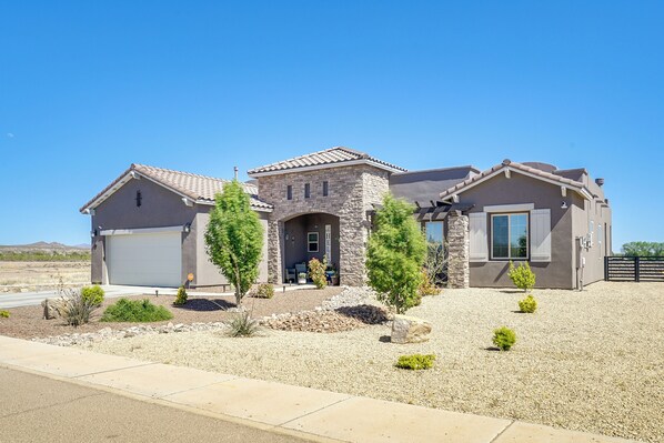 A modern two-story house with a stone facade, a garage, and a landscaped front yard with small trees and shrubs. - Las Cruces Home Rental w/ Organ Mountain Views! (Las Cruces)