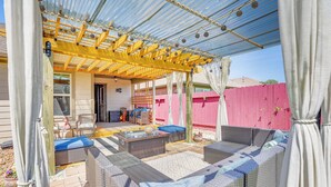 Une terrasse extérieure avec des meubles en osier, une pergola et une clôture rose.