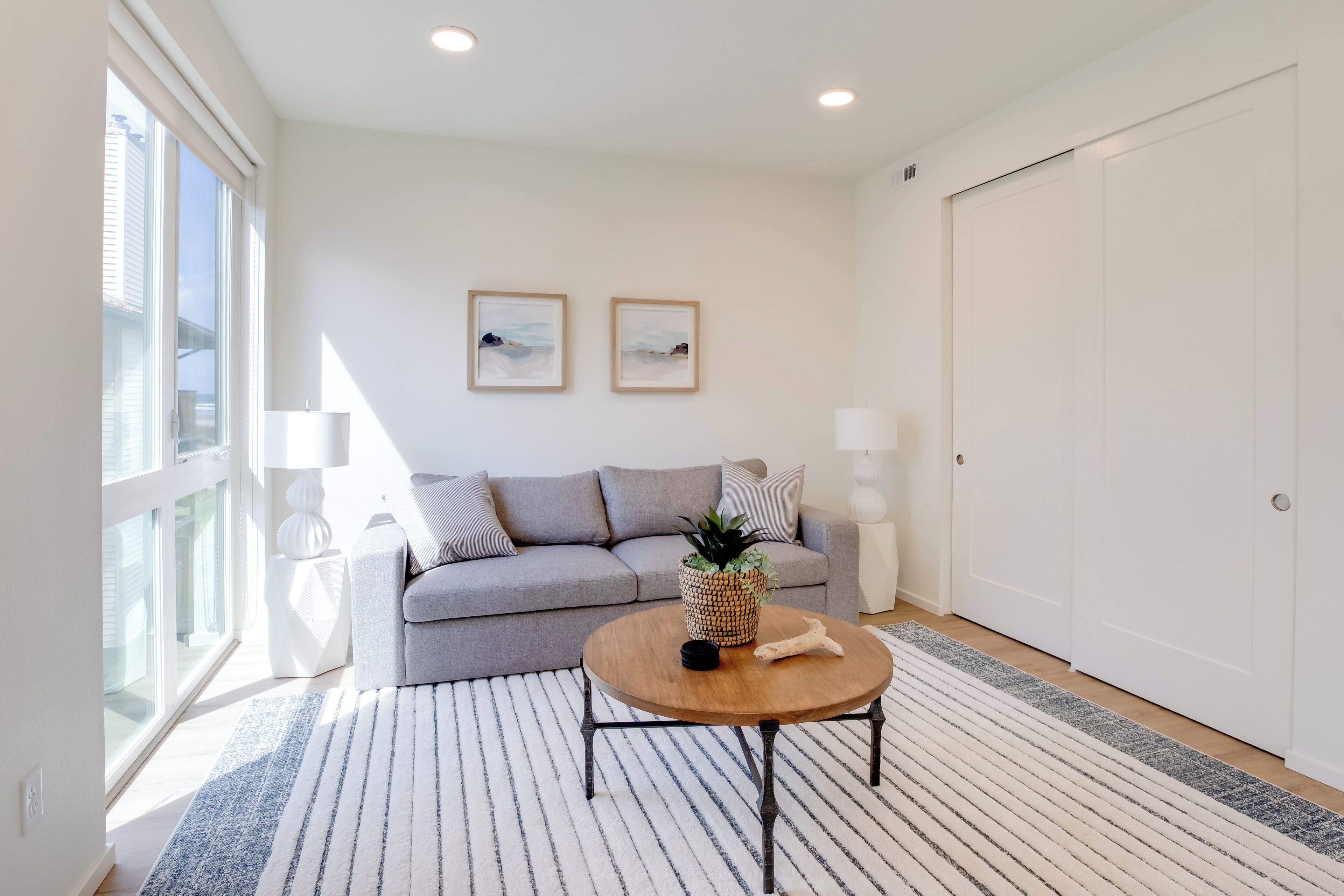 Ein modernes Wohnzimmer mit einem grauen Sofa, einem runden Couchtisch und zwei gerahmten Bildern an der Wand.