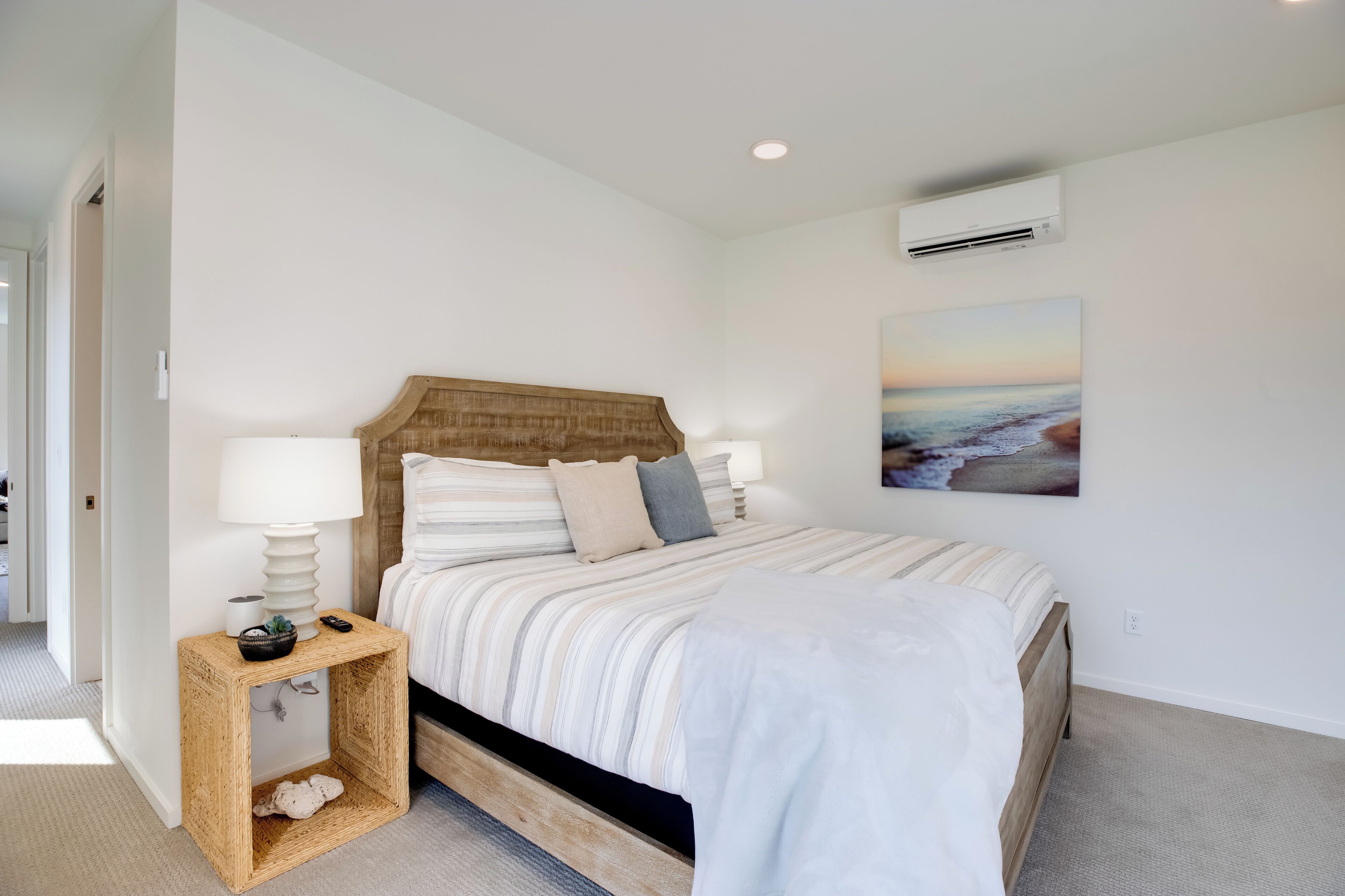A bedroom with a wooden headboard, a bed with striped bedding, a bedside table with a lamp, and a wall-mounted air conditioner.