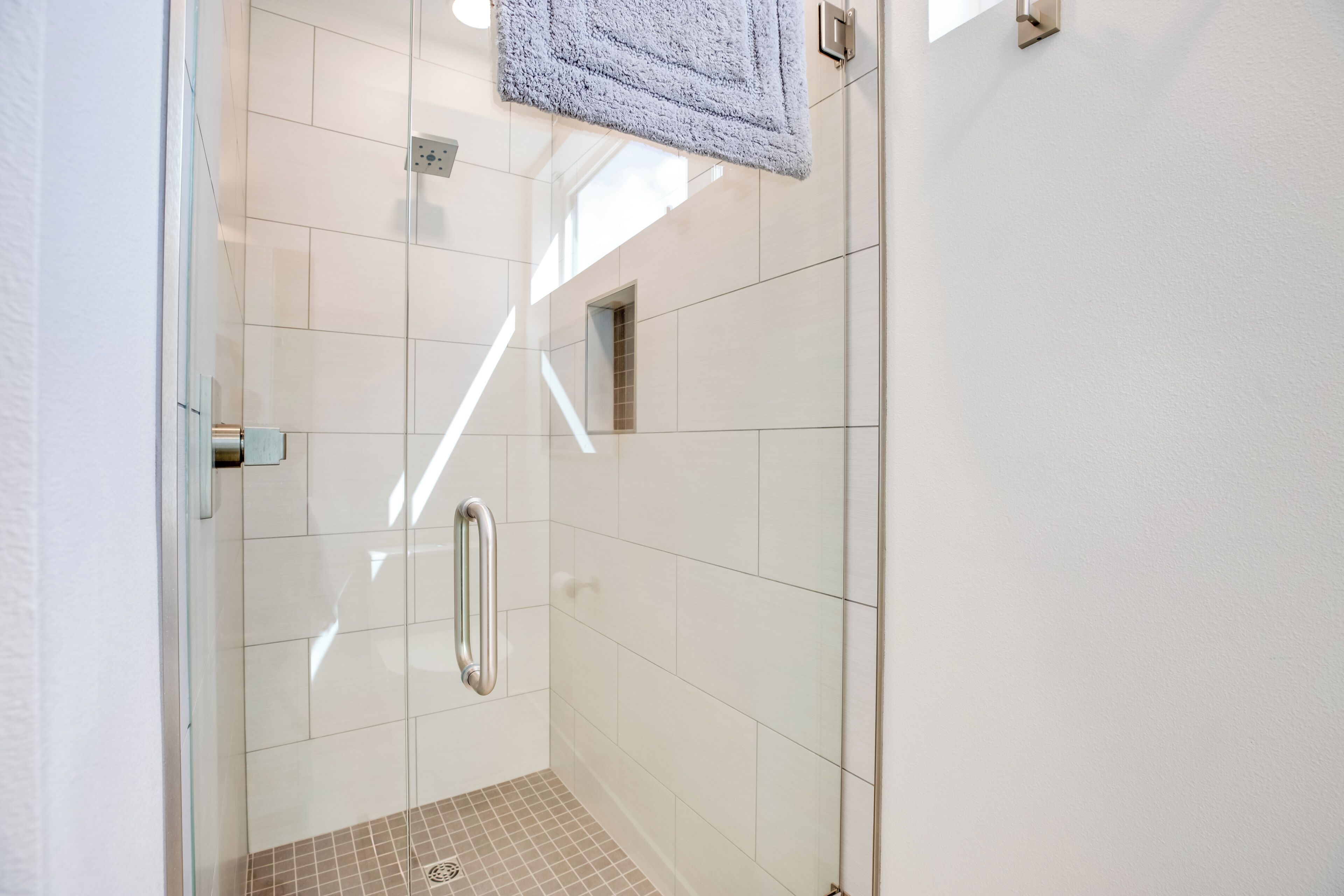 Un espace douche fermé par des parois de verre, doté d’un sol carrelé et d’une petite fenêtre.