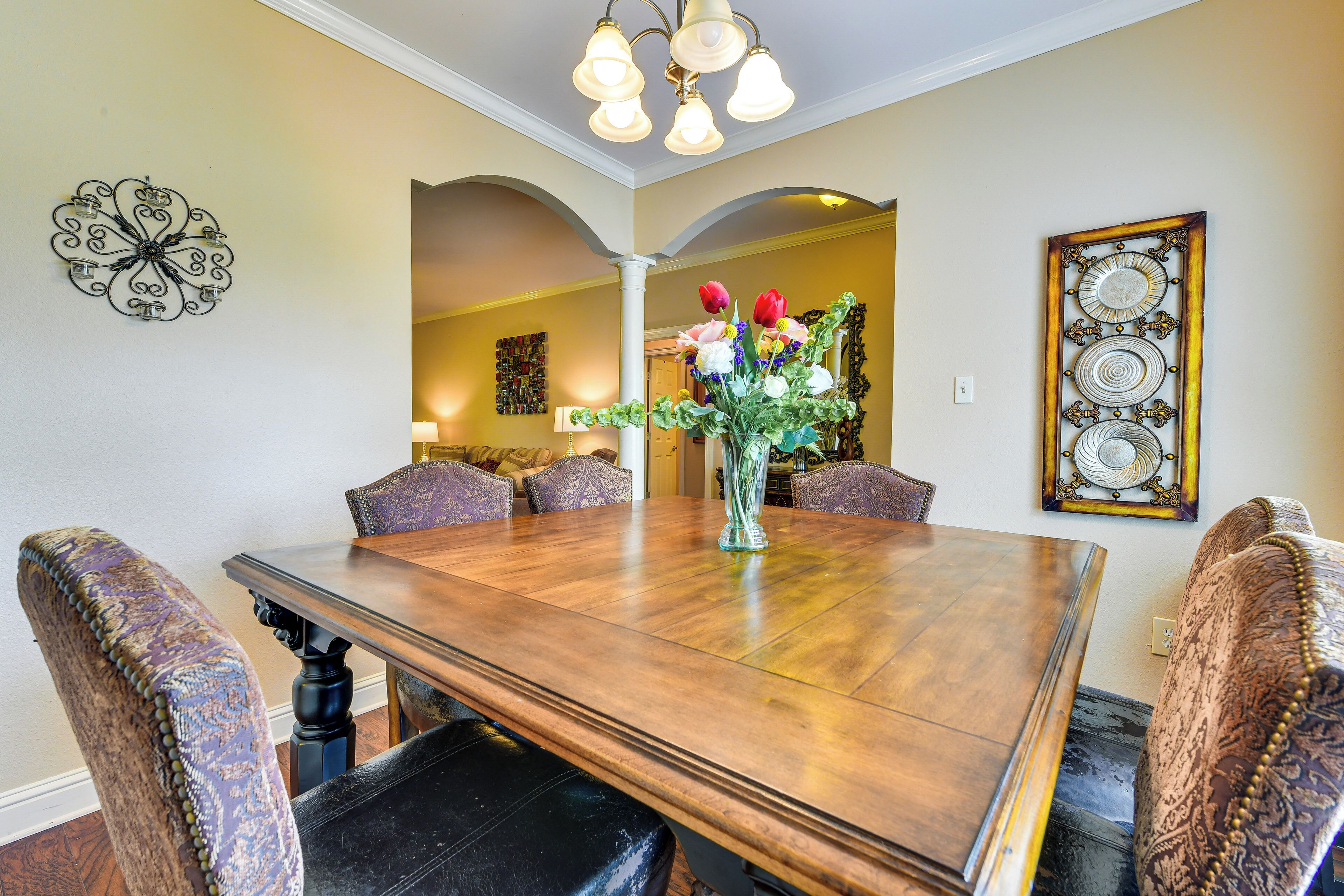 Un comedor con una mesa de madera, sillas estampadas, un florero con flores y decoración en las paredes.