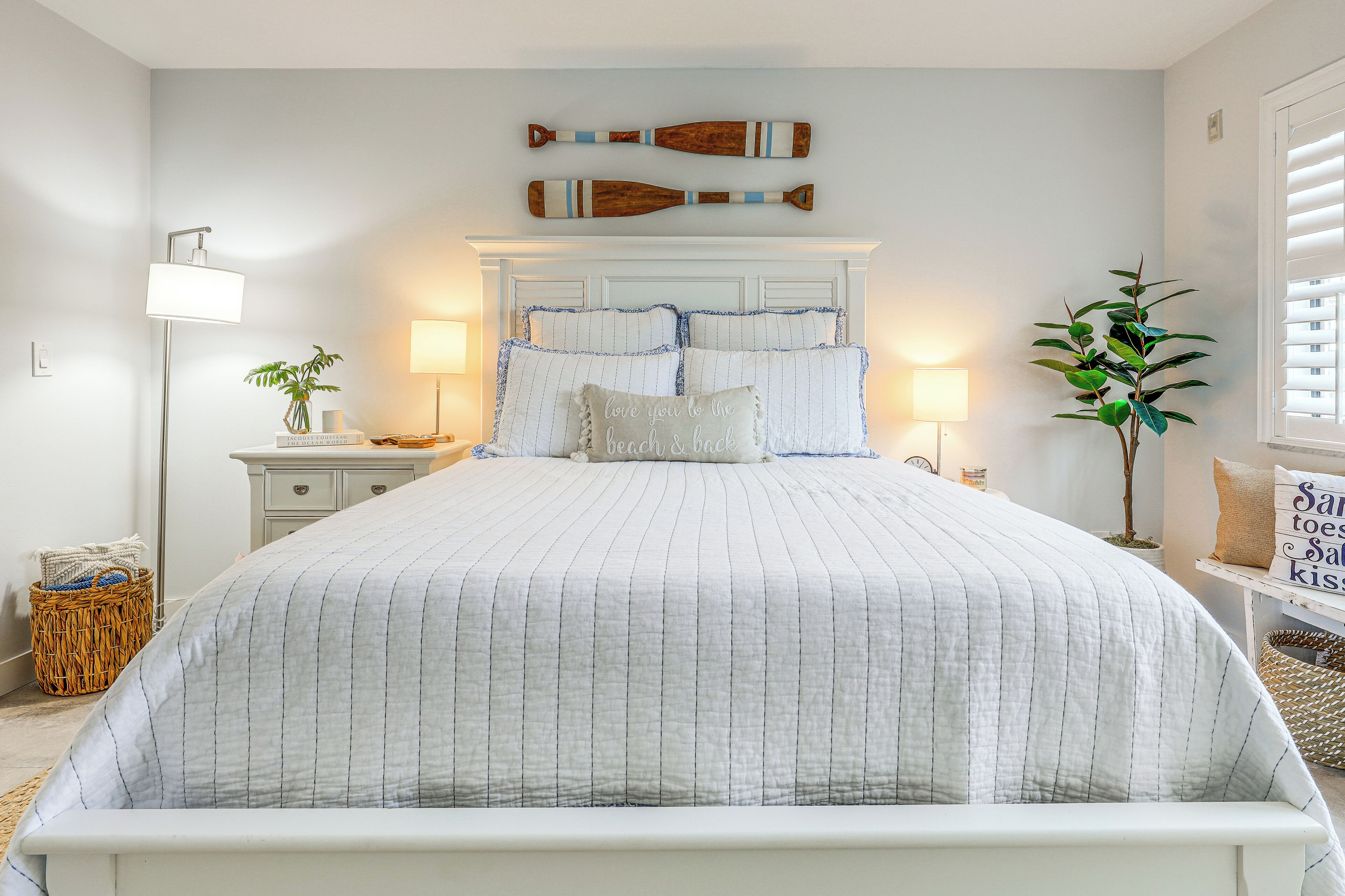 A neatly arranged bedroom with a large bed, two bedside tables, a floor lamp, and a potted plant.