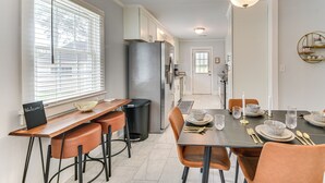 Une cuisine moderne avec un coin repas, comprenant un réfrigérateur en acier inoxydable, un comptoir-bar en bois et une table dressée avec des assiettes, des verres et des couverts.