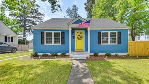 Une maison à deux étages avec une porte d’entrée jaune, un petit porche et un drapeau.