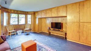 Een woonkamer met houten lambrisering, een televisie, een bank en twee stoelen.