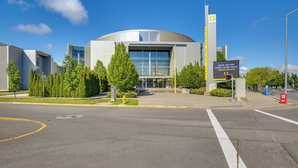 Een modern gebouw met een gebogen dak, grote ramen en een naambord.