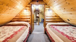 A cozy attic bedroom with wooden walls and two beds with floral bedding. - Island Park Cabin Getaway < 24 Mi to Yellowstone! (Island Park)