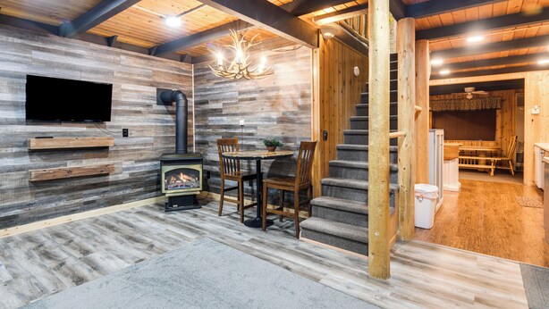 A cozy room with a fireplace, wooden walls, a television, and a staircase leading to another area. - Island Park Cabin Getaway < 24 Mi to Yellowstone! (Island Park)