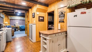 A cabin interior with wooden walls, a kitchen area including a refrigerator, a dining table, and a sofa. - Island Park Cabin Getaway < 24 Mi to Yellowstone! (Island Park)