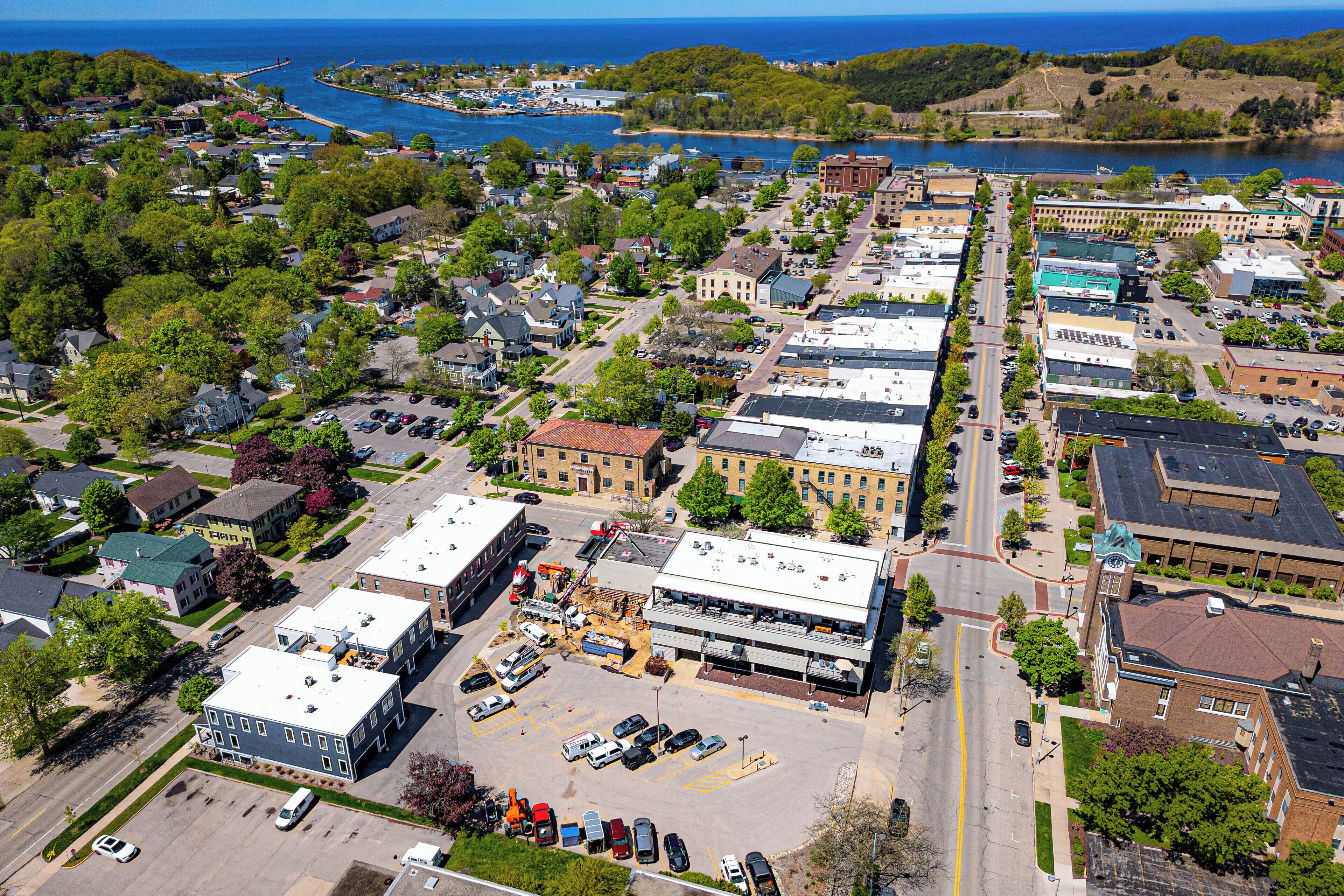An aerial view of a town with a mix of residential and commercial buildings, a parking lot, and a waterfront.