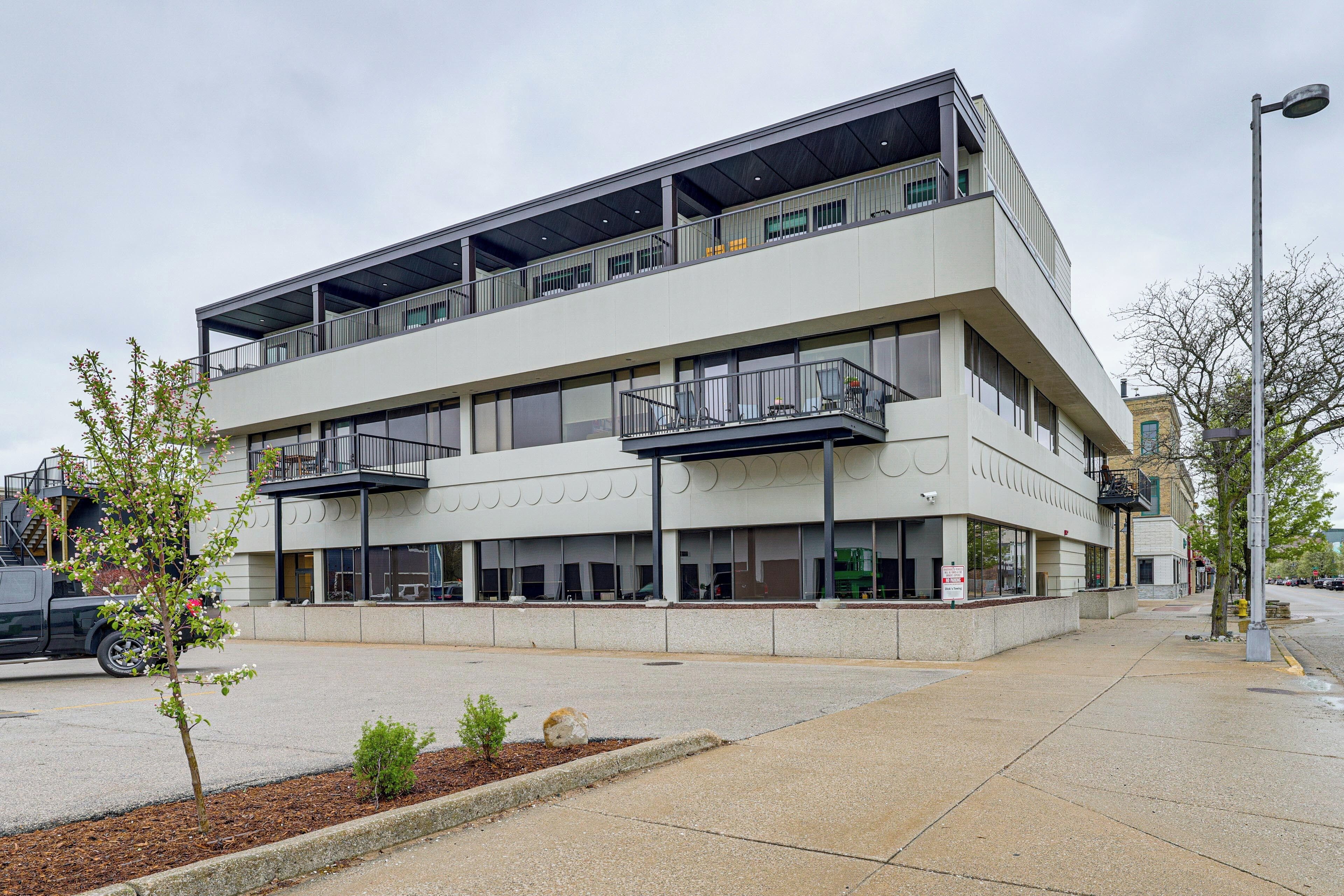 A multi-story building with balconies, a parking lot, and a sidewalk.