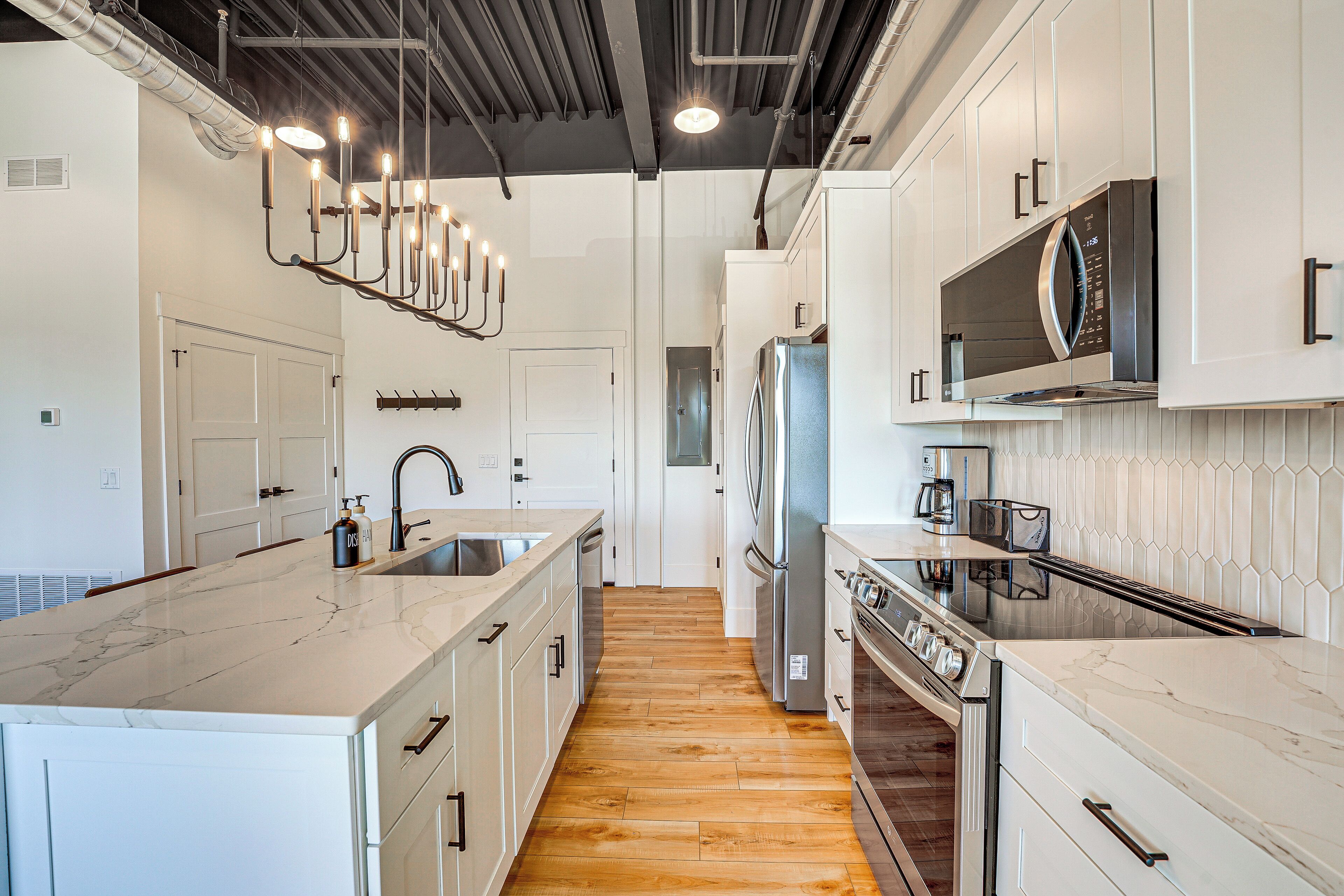 Una cocina moderna con armarios blancos, encimera de mármol, electrodomésticos de acero inoxidable y suelo de madera.