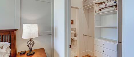 A bedroom with a wooden nightstand, a lamp, a bed, and a closet with shelves and drawers.