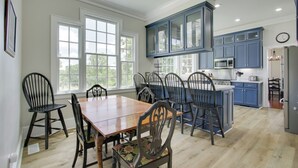 Cozinha espaçosa com mesa e cadeiras de madeira, armários azuis e uma janela grande que oferece iluminação natural.