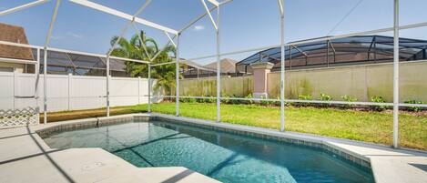 A swimming pool with a covered area, surrounded by a white fence and a grassy lawn.