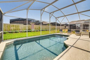 Une piscine dotée d’une zone abritée, entourée d’une clôture, et d’une terrasse avec des chaises.