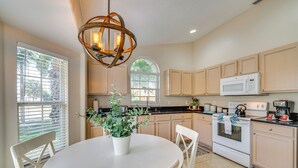 A kitchen with a round dining table, white chairs, a potted plant, a white stove, and wooden cabinets.