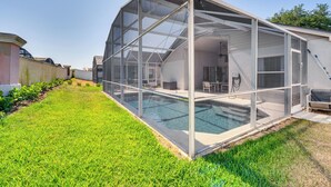 A covered outdoor swimming pool with a glass enclosure, surrounded by a well-maintained lawn.