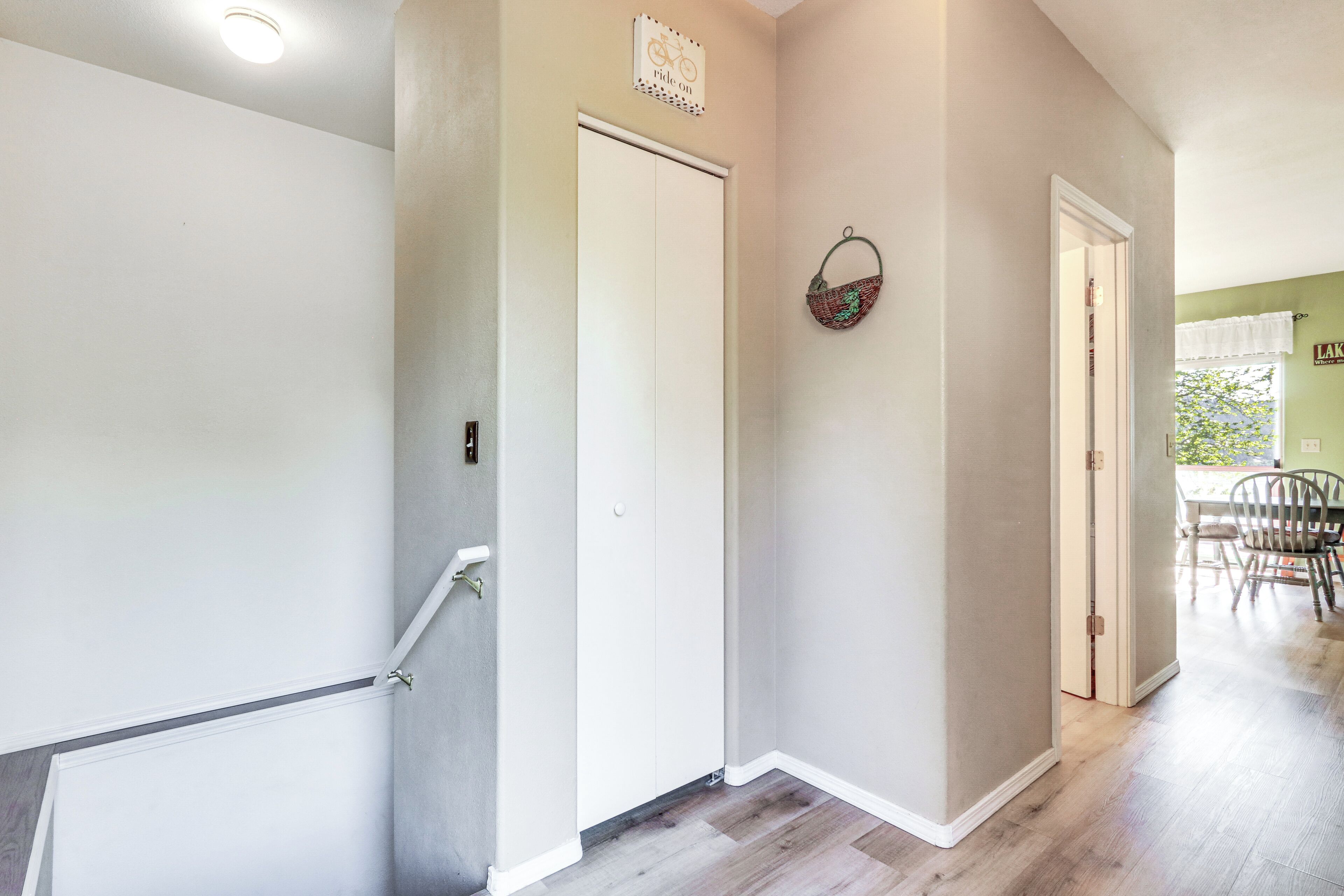 A hallway with a white door, a basket on the wall, and a dining area in the background.