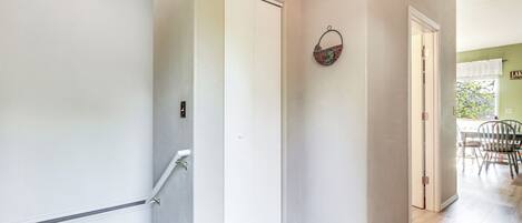 A hallway with a white door, a basket on the wall, and a dining area in the background.