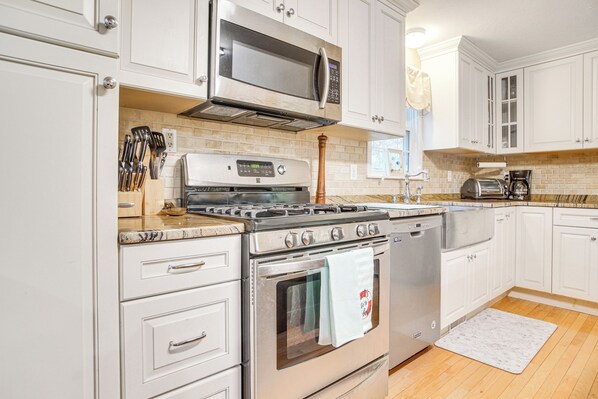 A kitchen with white cabinets, stainless steel appliances, and a wooden floor. - Beach & Lake Access: Group Getaway in Mashpee! (Mashpee)