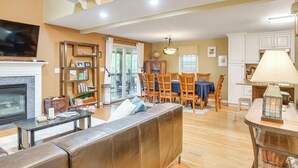 A spacious living area with a fireplace, a television, a dining table with chairs, and a kitchen area with cabinets and a refrigerator. - Beach & Lake Access: Group Getaway in Mashpee! (Mashpee)