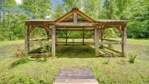 A wooden gazebo with a triangular roof and open sides, surrounded by lush greenery and a pond. - Winter Hiking + Hot Tub Soaks! Marion Mtn Cabin (Marion)