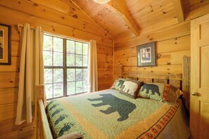 Ein Zimmer in einer Holzjagdhaus-ähnlichen Hütte mit großem Fenster, einem Bett mit einem gewölften Bär-Muster und einem gerahmten Bild an der Wand.