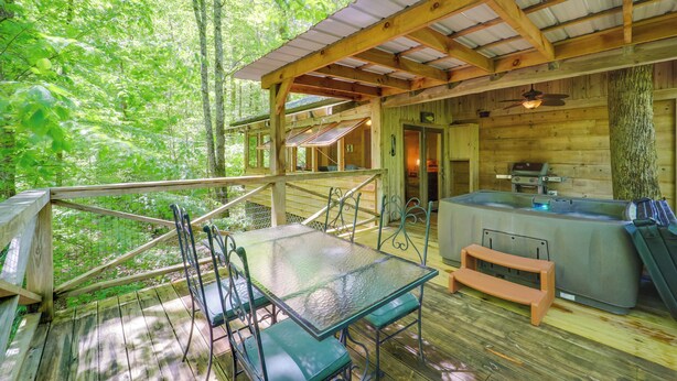 Een houten chalet met een glazen tafel en stoelen op een terras, een jacuzzi en uitzicht op het bos.