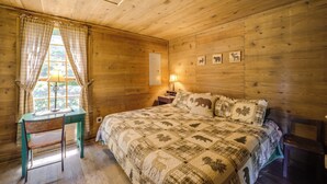 A wooden cabin room with a bed, a desk, and a window with curtains. - Hot Tub Haven! Blue Ridge Mountain Gem on 92 Acres (Marion)