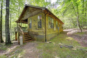 A wooden cabin with a porch and a staircase leading up to it, surrounded by trees.