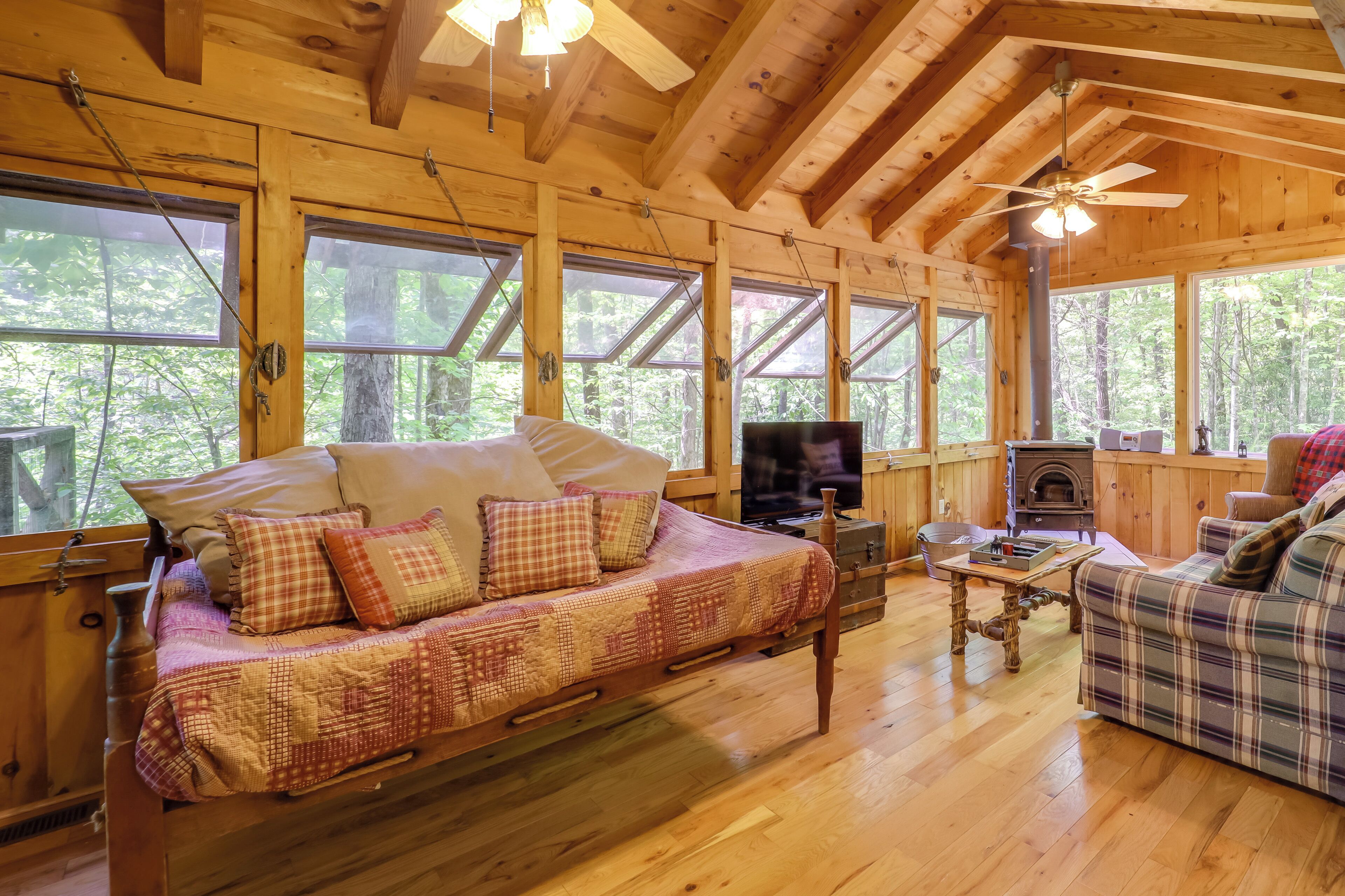 A cozy cabin interior with a wooden floor, a sofa, a television, and a fireplace.