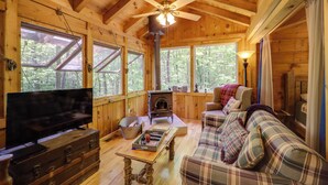 L’intérieur d’un chalet accueillant, avec un plafond en bois, une cheminée, un canapé, un téléviseur et de grandes fenêtres.