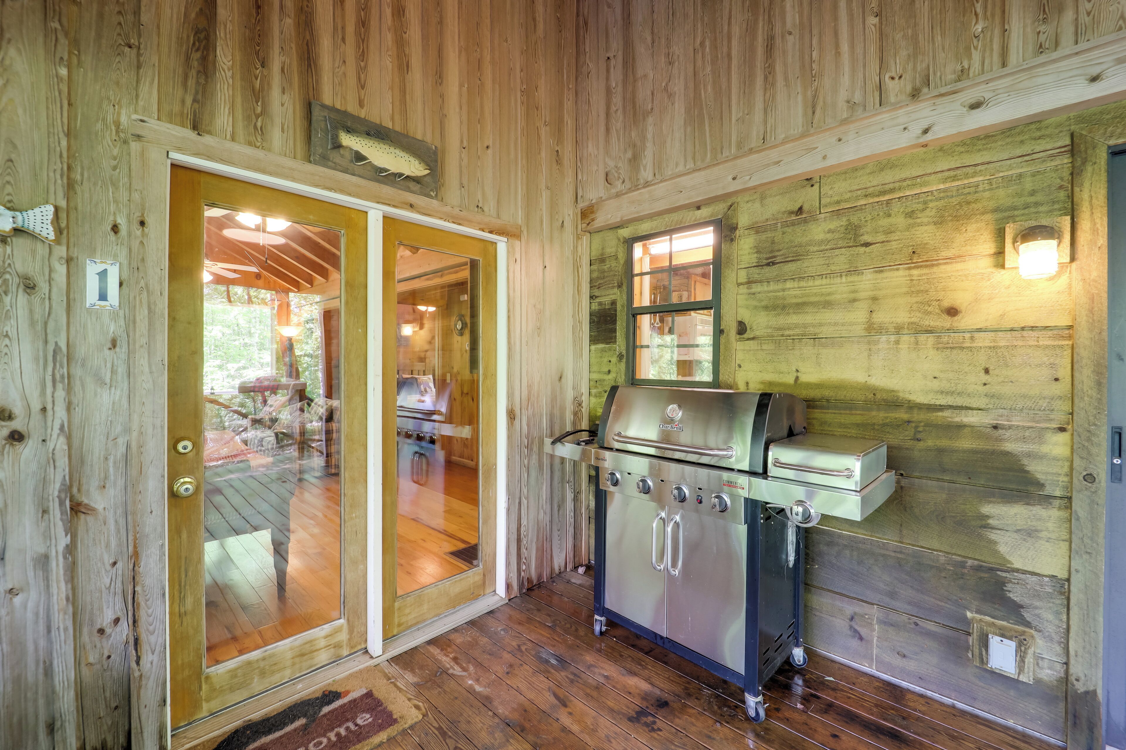 Interno di una baita in legno con una porta scorrevole in vetro che dà su un patio, una griglia in acciaio inox e un muro in legno con una finestra.