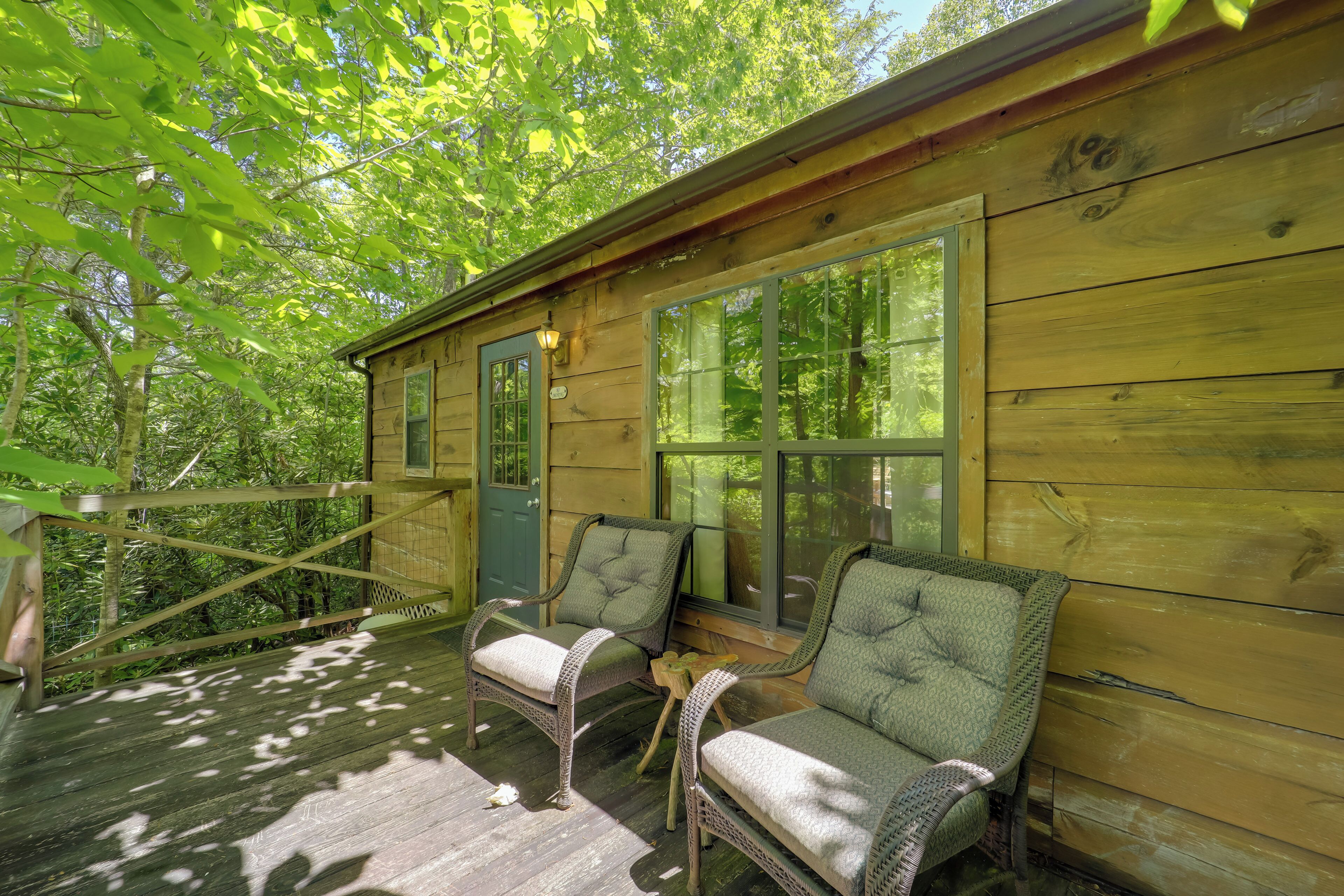 Een houten chalet met twee rieten stoelen en een kleine tafel op een veranda.