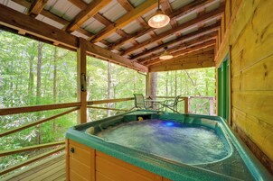 A wooden cabin with a hot tub, wooden deck, and a view of the forest.