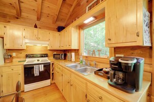 A wooden cabin kitchen with a stove, microwave, sink, and Keurig coffee maker.